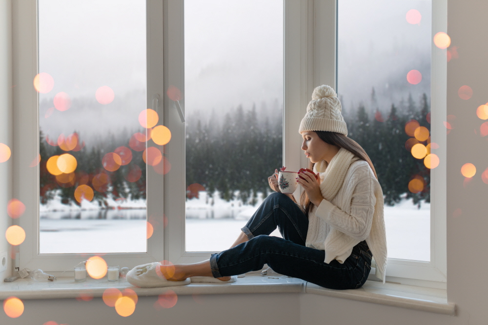 크기변환무료 사진 세련 된 흰색 니트 스웨터 스카프와 모자 뜨거운 차를 마시는 크리스마스 들고 컵을 들고 창턱에 집에 앉아 겨울 숲 배경